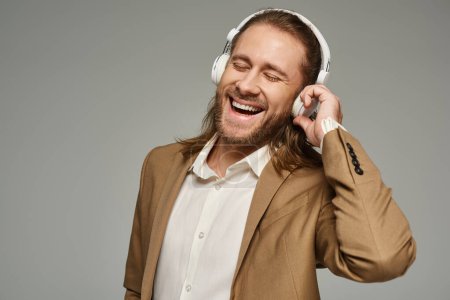 Photo for Amazed bearded businessman in headphones listening music on grey backdrop, formal attire - Royalty Free Image