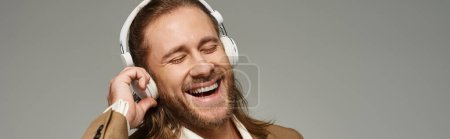 Photo for Cheerful bearded businessman in headphones listening music on grey backdrop, banner - Royalty Free Image