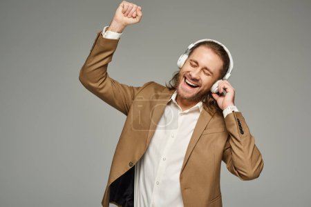 amazed bearded businessman in headphones listening music on grey backdrop, formal attire
