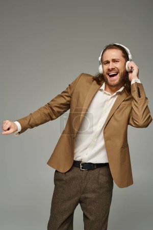 Photo for Excited and bearded businessman in headphones listening music on grey backdrop, formal attire - Royalty Free Image
