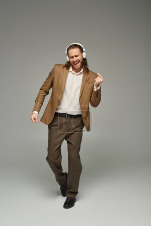 cheerful and bearded businessman in wireless headphones listening music on grey backdrop, dance