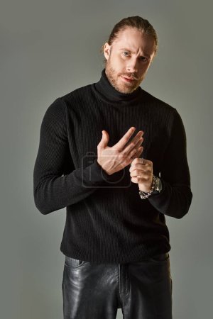 handsome bearded man in black turtleneck sweater wearing silver ring on finger on grey background