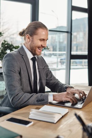 cheerful manager in formal wear typing on laptop while working on business project in office