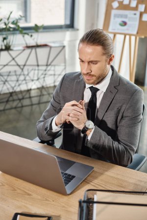 nachdenklicher Geschäftsmann im grauen Anzug, der am Arbeitsplatz im Büro auf das Notizbuch schaut, kreatives Denken