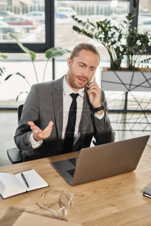 homme d'affaires sérieux regardant ordinateur portable lors d'une conversation sur smartphone sur le lieu de travail dans le bureau