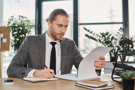 Photo for Focused businessman in grey suit looking in notebook during paperwork at workplace in office - Royalty Free Image