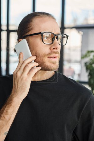 portrait of stylish businessman in eyeglasses talking on mobile phone and looking away in office