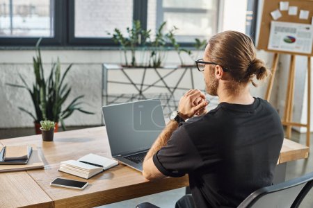 back view of manager in black t-shirt near laptop with blank screen on work desk in modern office