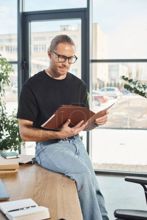 homme d'affaires en lunettes assis sur le bureau et regardant dans le dossier avec des documents dans le bureau