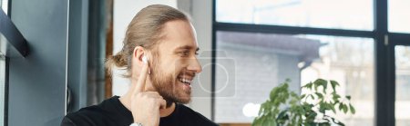 stylish successful businessman smiling while listening music in wireless earphone in office, banner