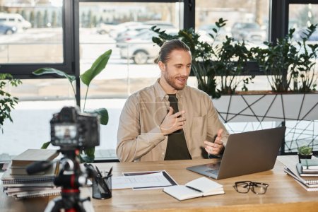 successful businessman talking near laptop and digital camera while during video blog in office