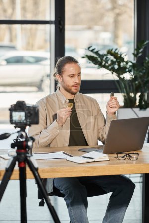 homme d'affaires confiant tenant Bitcoins lors d'un appel vidéo sur un ordinateur portable devant un appareil photo numérique