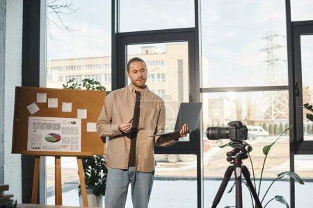 businessman with laptop talking near flip chart with analytics and digital camera in modern office
