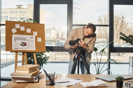 hombre de negocios creativo ajustando la cámara digital cerca del rotafolio con análisis y escritorio en la oficina