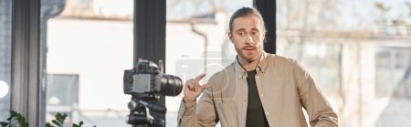 Geschäftsmann spricht und gestikuliert nahe Digitalkamera während Videoblog im Büro, horizontales Banner