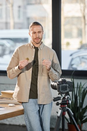 Foto de Ambicioso hombre de negocios mostrando bitcoins delante de la cámara digital en la oficina, marketing de inversión - Imagen libre de derechos