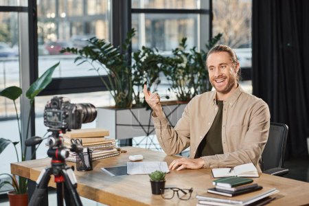 glücklicher erfolgreicher Geschäftsmann spricht und gestikuliert während Videoblog am Schreibtisch mit Notizbüchern