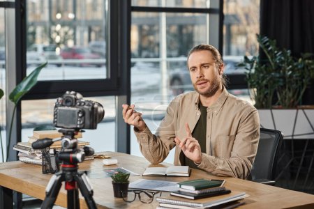 Seriöser Unternehmer spricht und gestikuliert vor Digitalkamera während Videoblog im Büro