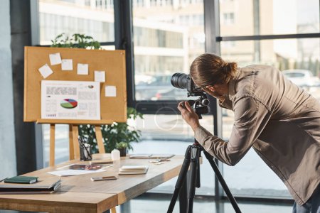 Kreativ-Manager justiert Digitalkamera nahe Korkboard mit Grafiken für Präsentation im Büro