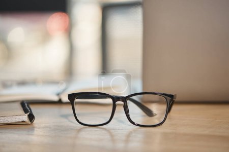 stylish eyeglasses on work desk in contemporary office on blurred background, business fashion