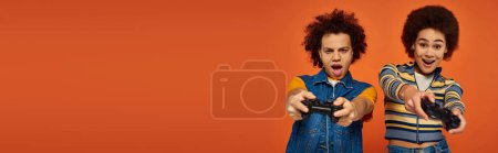 cheerful young african american brother and sister playing video games with joysticks, banner