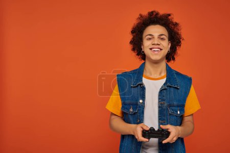 young handsome african american man emotionally playing video games with joystick on orange backdrop