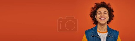 handsome african american man in urban attire posing emotionally on orange backdrop, banner