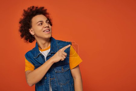 handsome young african american man in casual urban attire posing actively on orange background
