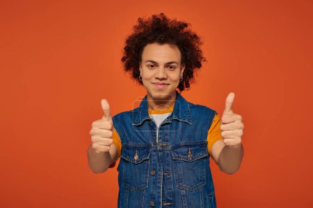 handsome young african american man in casual urban outfit posing emotionally on orange background