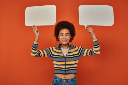 joyful african american woman in vibrant attire posing with speech bubbles and smiling at camera