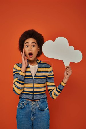 attractive african american woman in stylish attire posing with thought bubble on orange backdrop