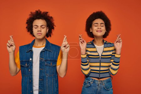 young attractive african american siblings posing together and making wish on orange backdrop