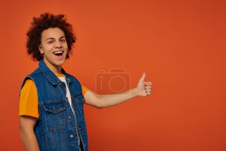 bel homme heureux afro-américain en tenue urbaine gesticulant activement sur fond orange