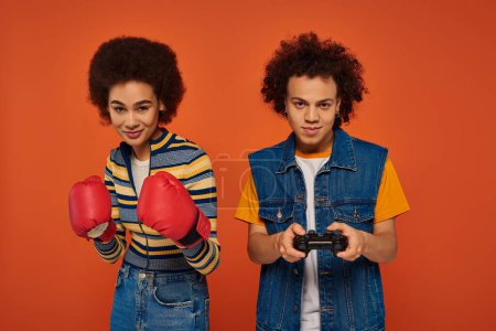 happy african american woman in boxing gloves posing next to her brother with joystick, family