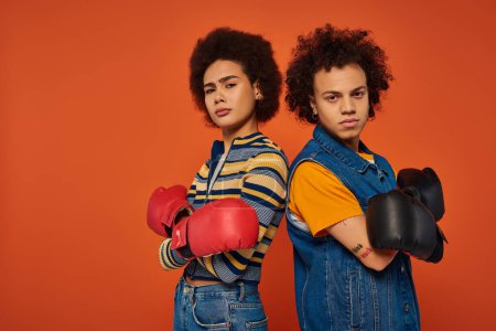 sportliche afrikanisch-amerikanische Geschwister in Boxhandschuhen haben gemeinsam Spaß auf orangefarbenem Hintergrund, Familie