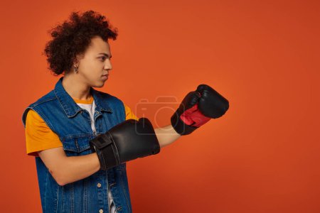 good looking athletic african american man posing lively in boxing gloves on orange background