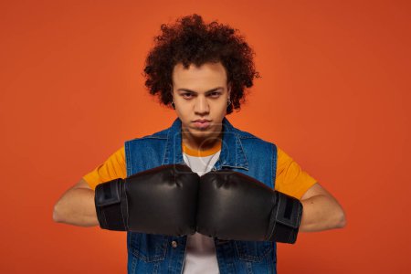 Foto de Buen aspecto deportivo afroamericano hombre posando activamente en guantes de boxeo sobre fondo naranja - Imagen libre de derechos