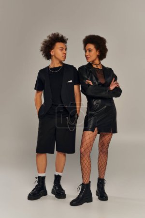 attractive stylish african american siblings in fashionable black outfits posing on gray backdrop