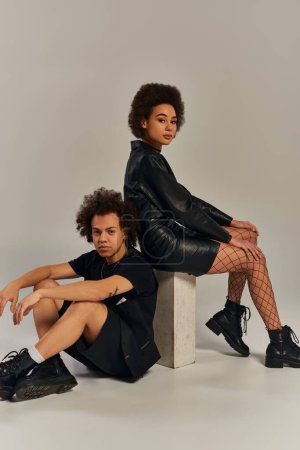 stylish fashionable african american siblings posing together and sitting on gray backdrop, family