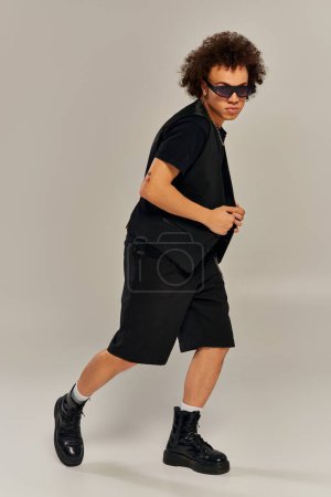 Foto de Guapo modelo masculino afroamericano de moda con gafas de sol elegantes posando activamente en la cámara - Imagen libre de derechos
