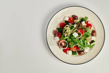 Foto von oben: Teller mit frisch zubereitetem traditionellen griechischen Salat auf grauem Hintergrund, gesunde Ernährung