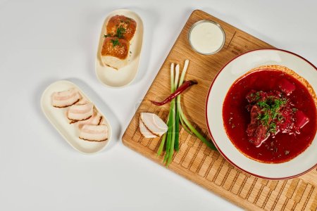 traditional Ukrainian borsch soup near garlic buns, pork lard and sour cream on wooden cutting board