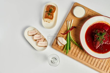 Foto de Rico sabor borsch ucraniano cerca de bollos de ajo, manteca de cerdo y crema agria en tabla de cortar de madera - Imagen libre de derechos
