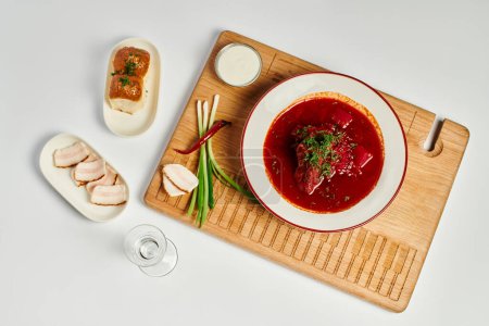 traditional Ukrainian beetroot soup near garlic buns, pork lard and sour cream on cutting board