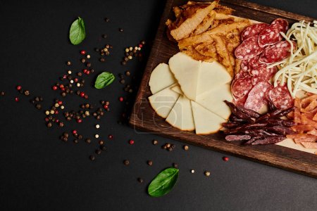 top view of charcuterie board with delicious cheese selection, dried beef and salami slices on black