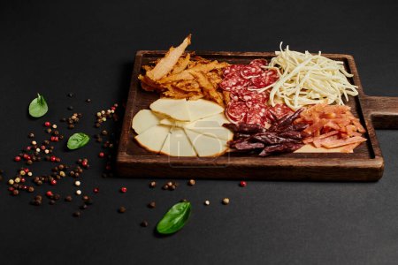 top view of charcuterie board with cheese selection, dried beef and salami on black, antipasto