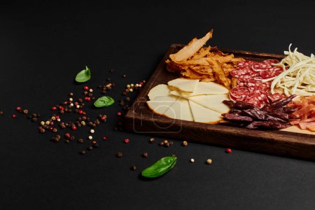 charcuterie board ou cuisine de fête avec sélection de fromages gastronomiques, boeuf séché et tranches de salami sur fond noir