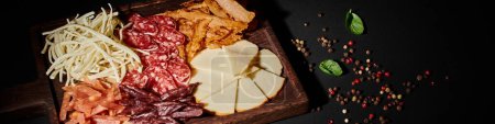bannière de planche de charcuterie avec sélection de fromages gastronomiques, tranches de boeuf séché et salami sur fond noir