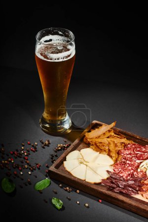 szklanka piwa rzemieślniczego w pobliżu deski z serem dla smakoszy, suszoną wołowiną i salami na pokładzie