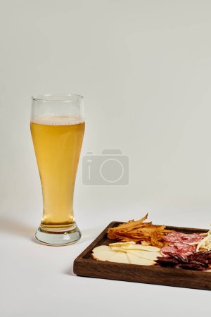 glass of craft beer near charcuterie board with cheese selection, dried beef and salami on grey